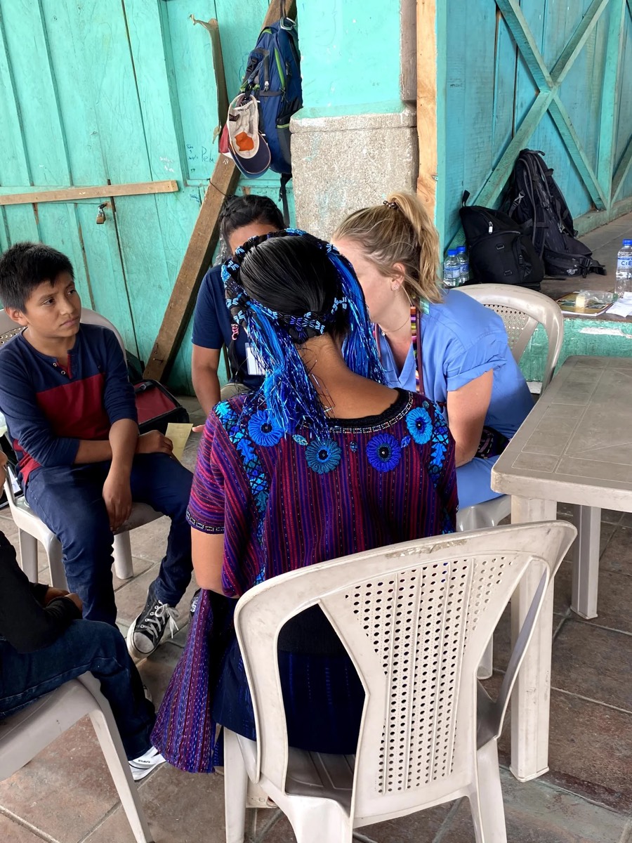 A volunteer sits with a woman in traditional Guatemalan dress during a clinic visit